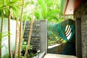 Modern outdoor shower with tropical plants and a stone wall.