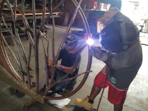 Two workers welding metal sculpture together.
