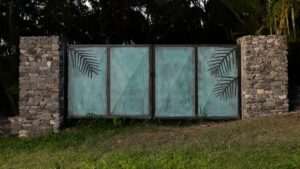 A blue-green metal fence with palm leaf shadows on grass.