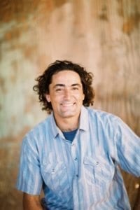 Smiling man with curly hair wearing a blue shirt.