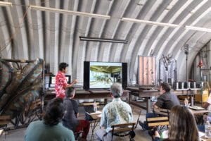 People attending a presentation in a rustic indoor setting with a projector screen.