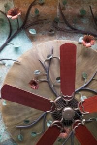 A ceiling fan with wooden blades and decorative flowers.