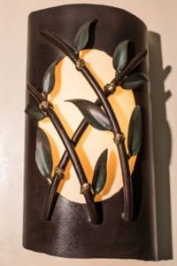 Decorative wall sconce with a warm glowing light behind metal leaves.