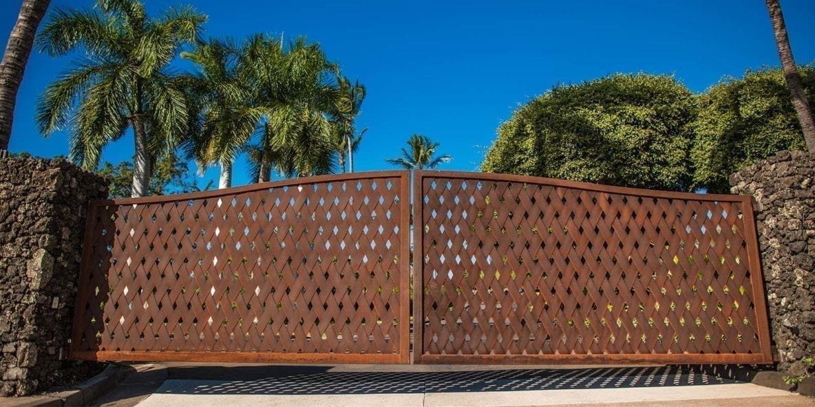 Decorative wooden driveway gate with lattice design under a clear blue sky.
