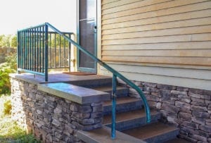 Curved metal handrail beside stone steps leading to a porch.