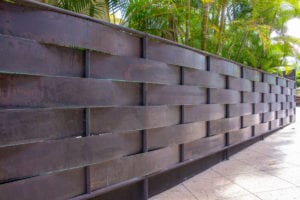 Modern dark brown woven-style brick wall with plants in the background.