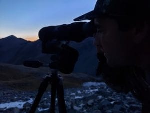 Person using a telescope outdoors during twilight.