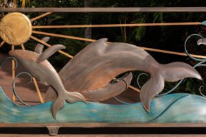 Wooden sculpture of two dolphins jumping over waves.