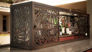 Decorative wooden wine rack with carved leaf patterns holding several wine bottles.