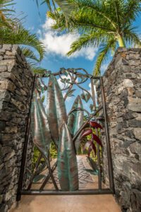 Artistic metal gate between stone pillars under palm trees.