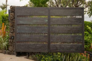 A dark wooden fence with horizontal slats and greenery behind it.