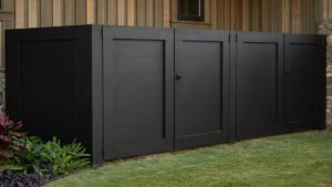 Modern black wooden garden fence with a gate on a green lawn.