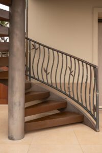 Curved wooden staircase with wrought iron railing and vertical pillar.