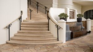 Elegant curved staircase with wrought iron railing and beige carpet.