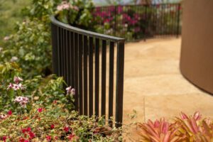 Black metal fence curving around a garden path with flowers.