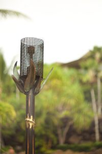 Outdoor tiki torch with a protective mesh, set against a blurred green background.