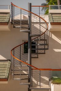 A modern spiral staircase with metal steps and wooden handrails against a beige wall.