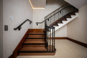 Modern wooden staircase with black metal railing in a well-lit hallway.