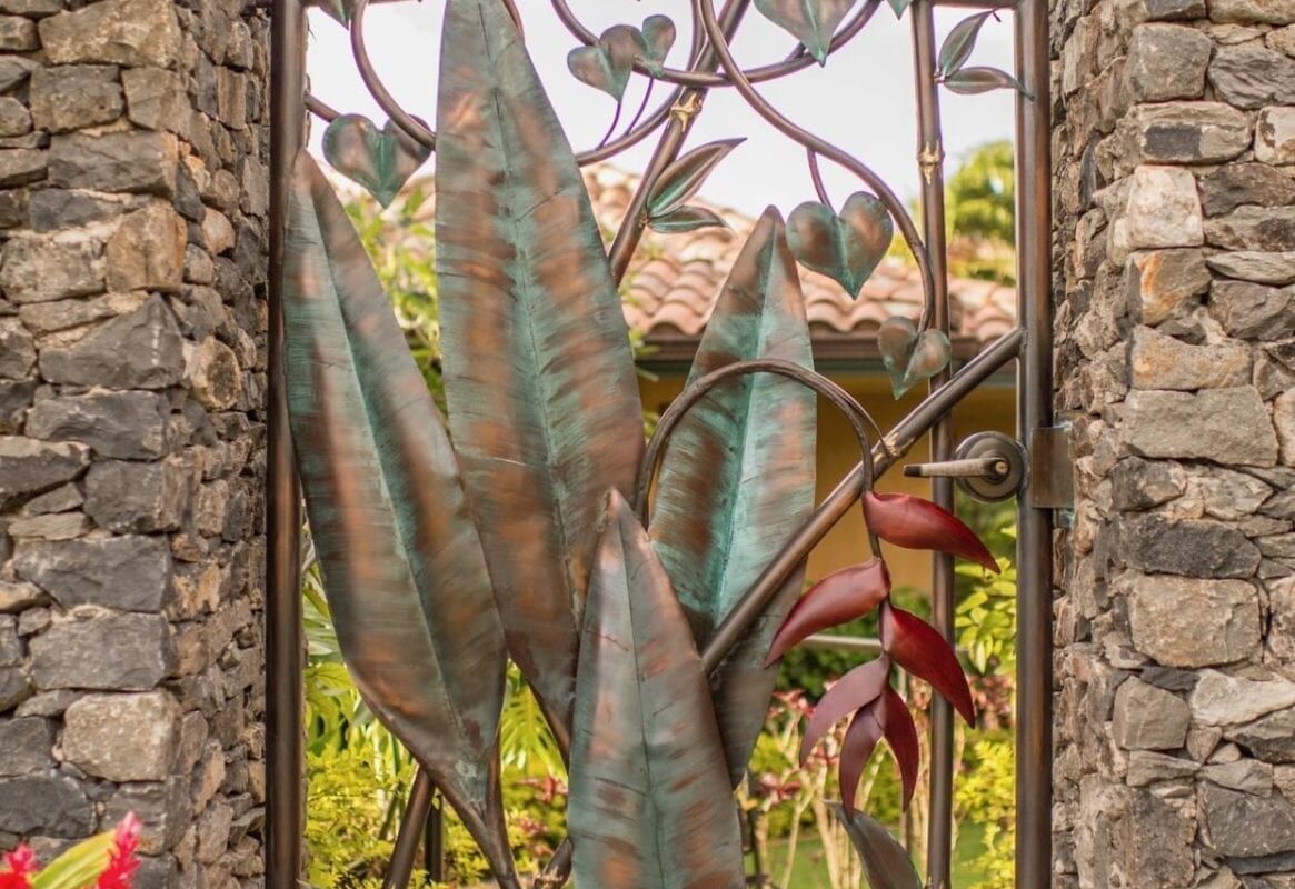 A decorative metal gate with tree and leaf designs between stone pillars.