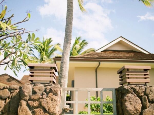 Tropical house with stone fence and palm trees under a clear sky.
