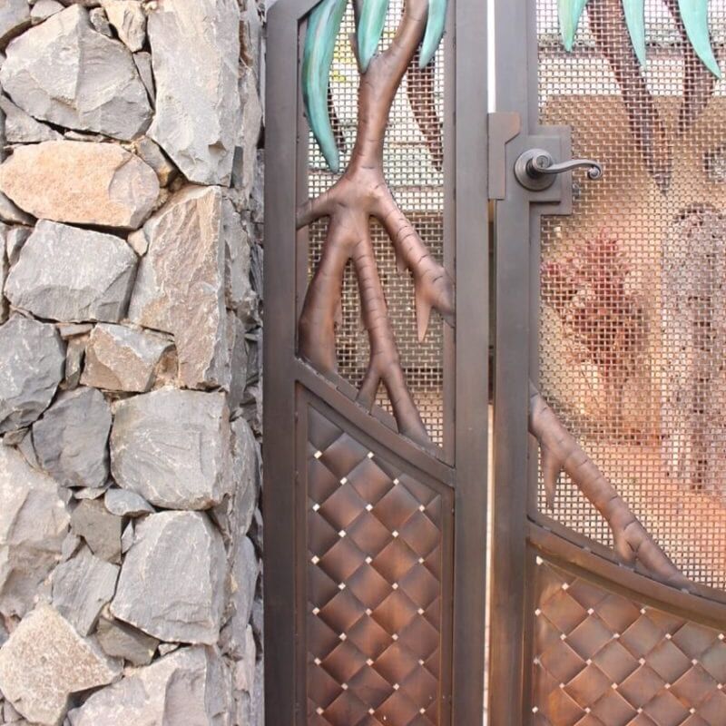 Intricately designed metal door with organic, tree-like patterns beside a stone wall.