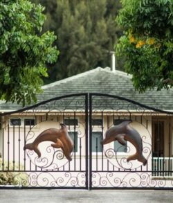 #31 Gate with artistic dolphins in front of a house surrounded by trees.