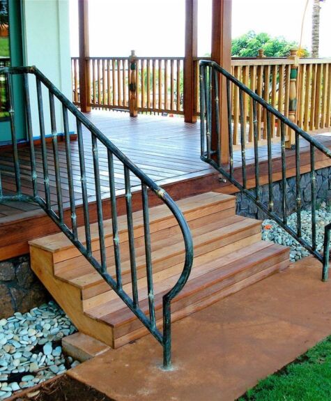 Wooden porch steps with black wrought iron railings and stone pathway.