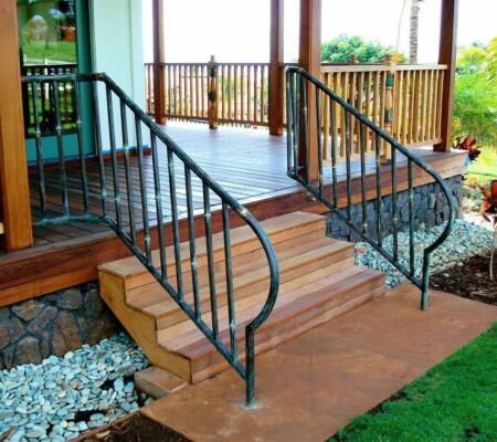 Wooden porch stairs with decorative black metal railings and stone landscaping.