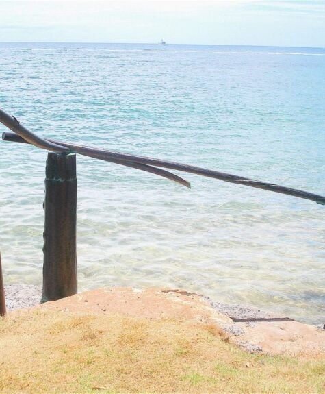 Rustic wooden railing overlooking clear ocean water and sandy shore.