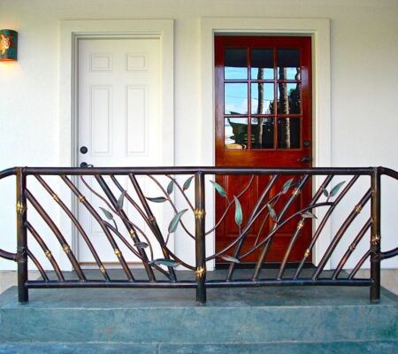 Decorative metal railing with a botanical design in front of a red door and white wall.