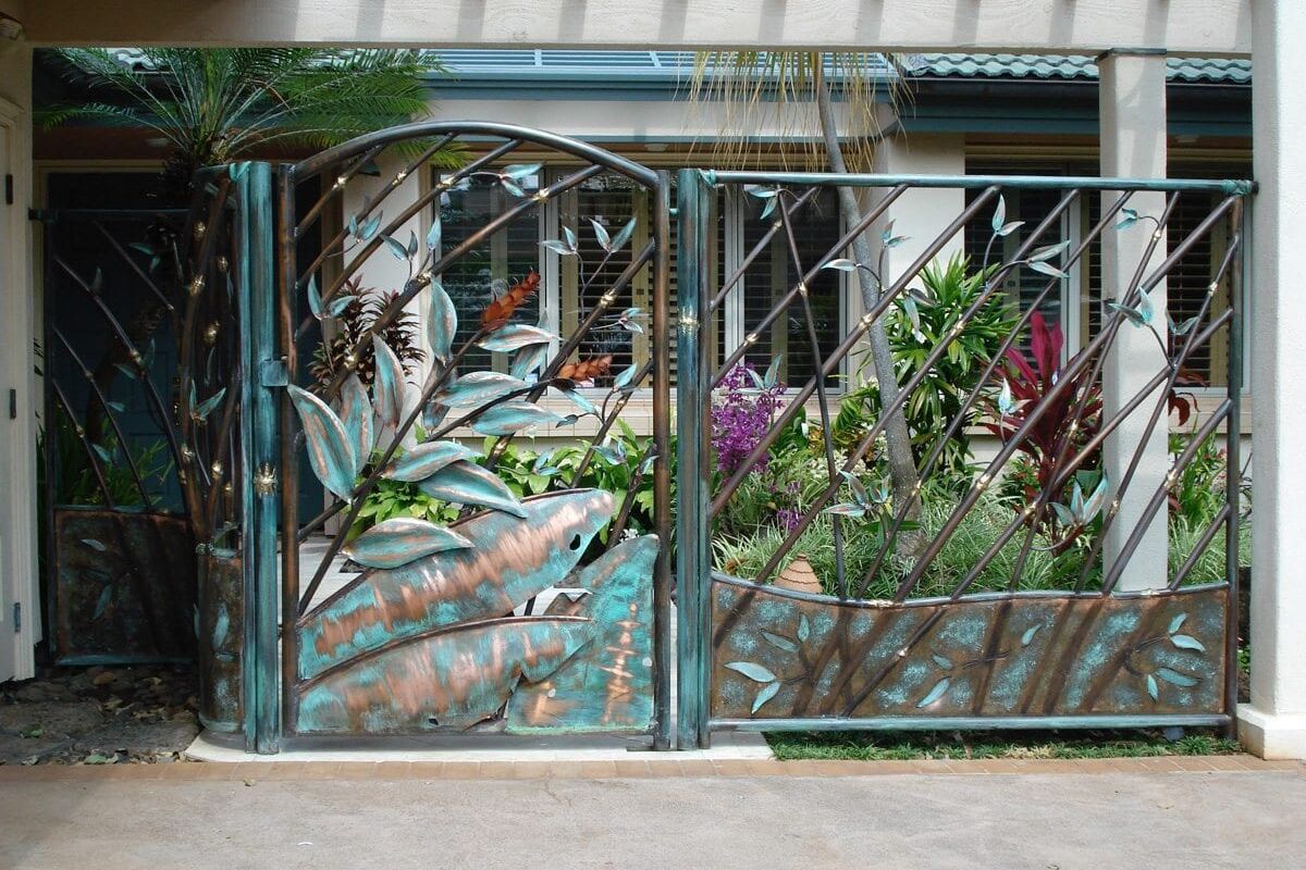Decorative metal gate with a nature-inspired design in front of a garden.
