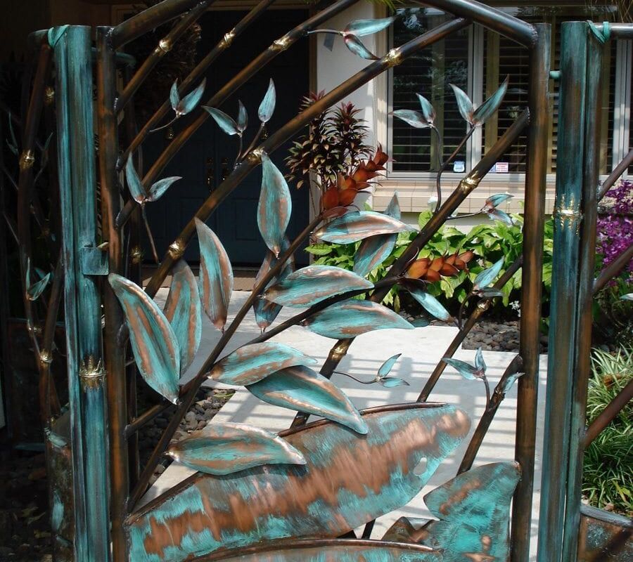Decorative metal gate with leaf design near a garden path.