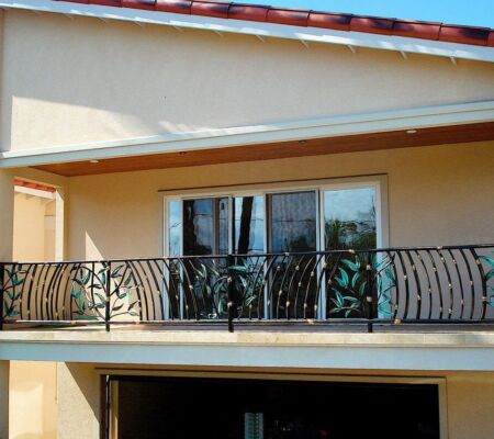 Balcony with intricate wrought iron railing on a beige house.