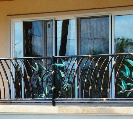 Decorative black metal balcony railing with plant motifs on a beige building.
