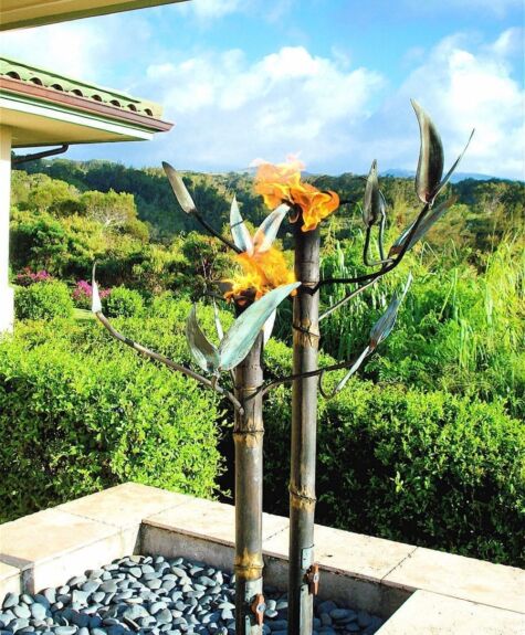 Two metal bird sculptures with orange flowers on tall poles in a garden.