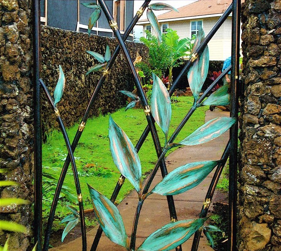 Decorative metal gate with leaf patterns opening to a lush garden.