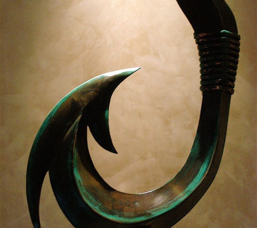 A carved greenstone fish hook pendant with a polished finish.