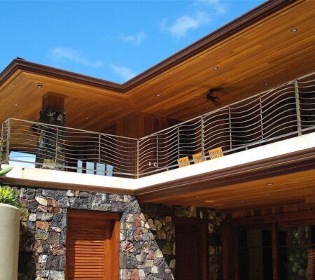 Modern house balcony with wooden ceiling and stone walls under blue sky.