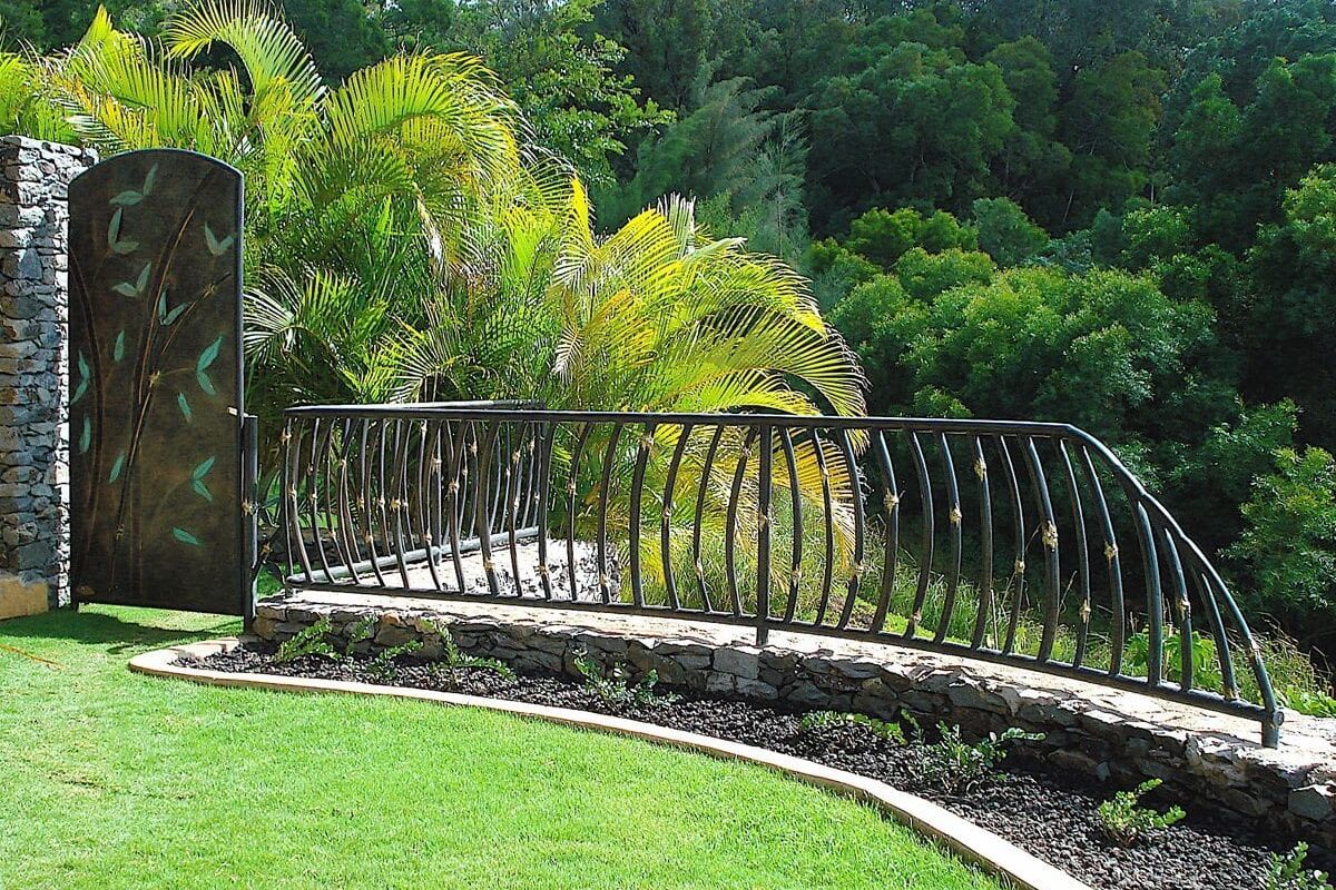 A curved stone wall with iron railing overlooking lush greenery.