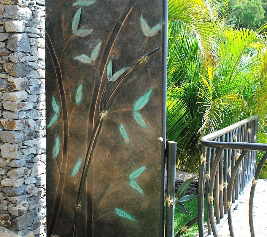 Decorative metal door with butterfly designs and tropical greenery outside.