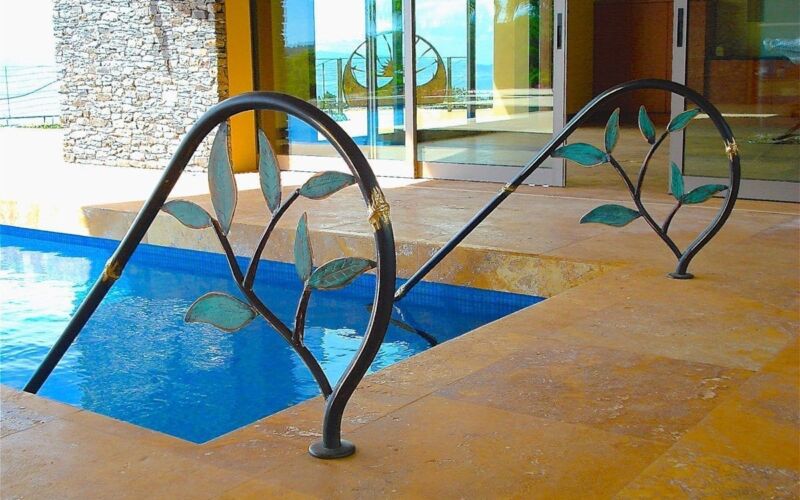 Modern outdoor pool with artistic metal railings and stone flooring.