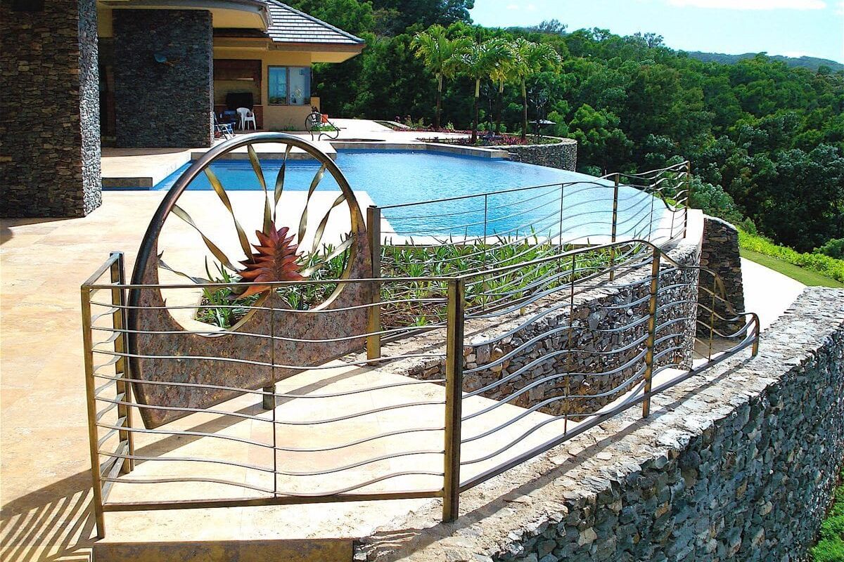 Stone patio and pool area with metal fence and decorative wheel.