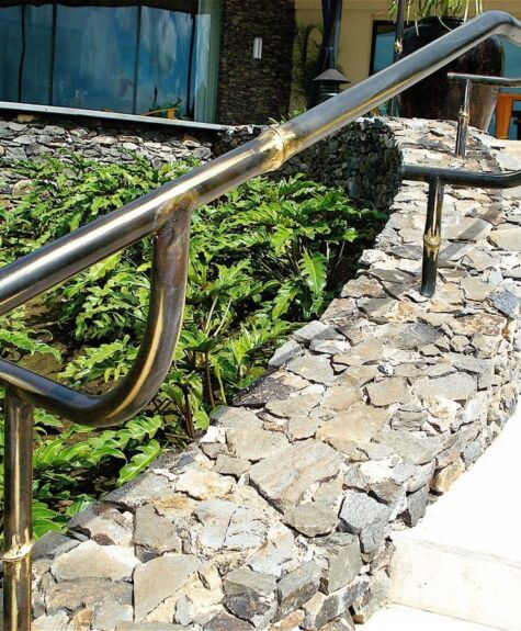 Metal handrails along a stone pathway with greenery in the background.