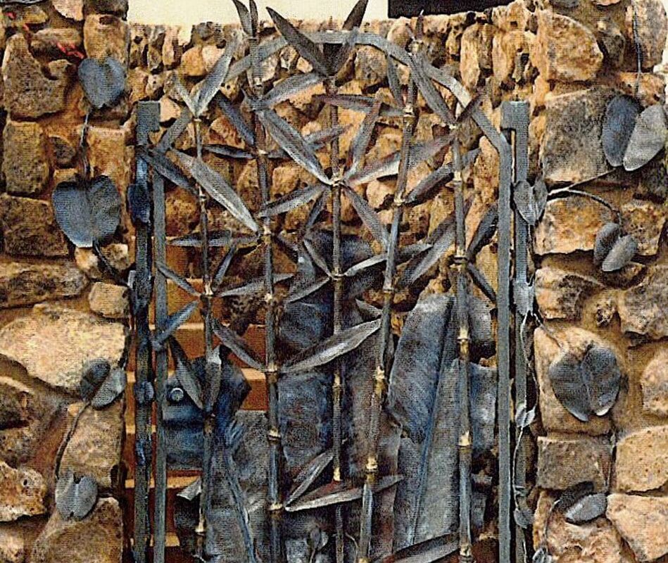 Intricate metal gate with leaf motifs against a rustic stone wall.