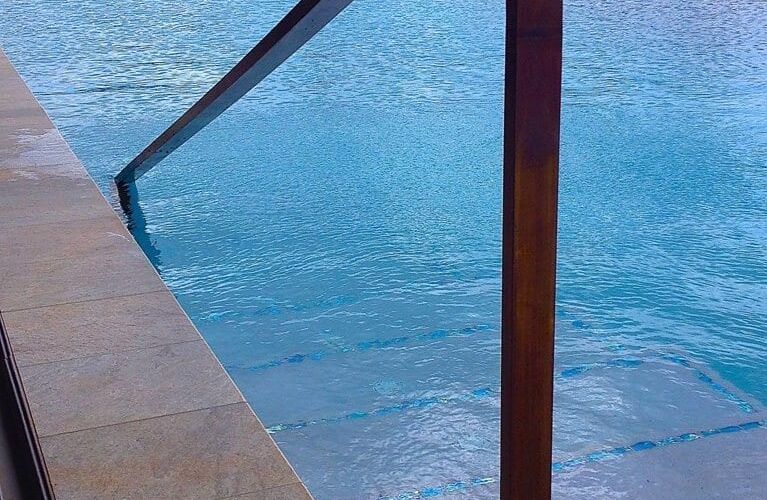 Clear swimming pool with metal handrail and stone deck.