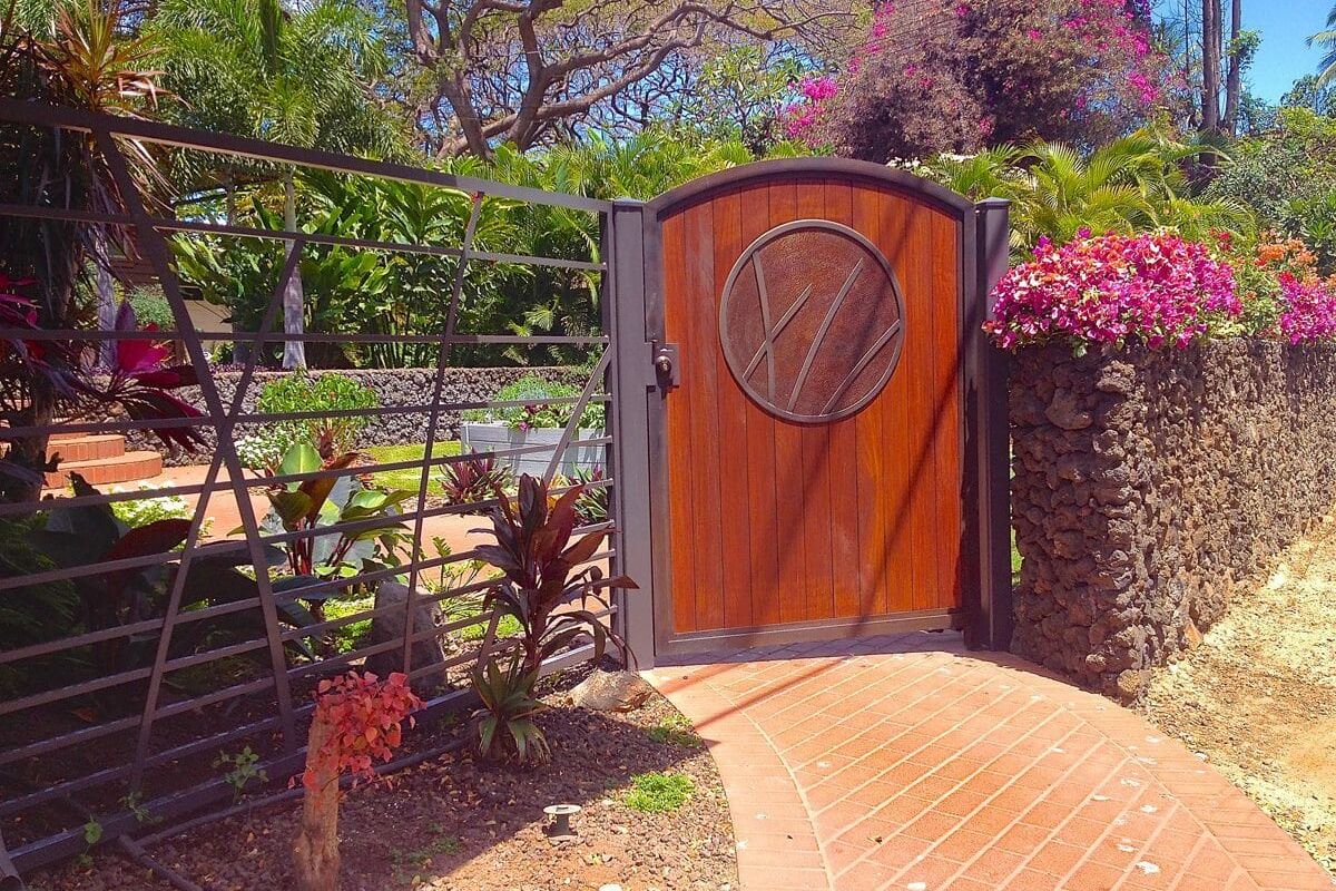 Decorative arched wooden gate with a circular emblem in lush garden.