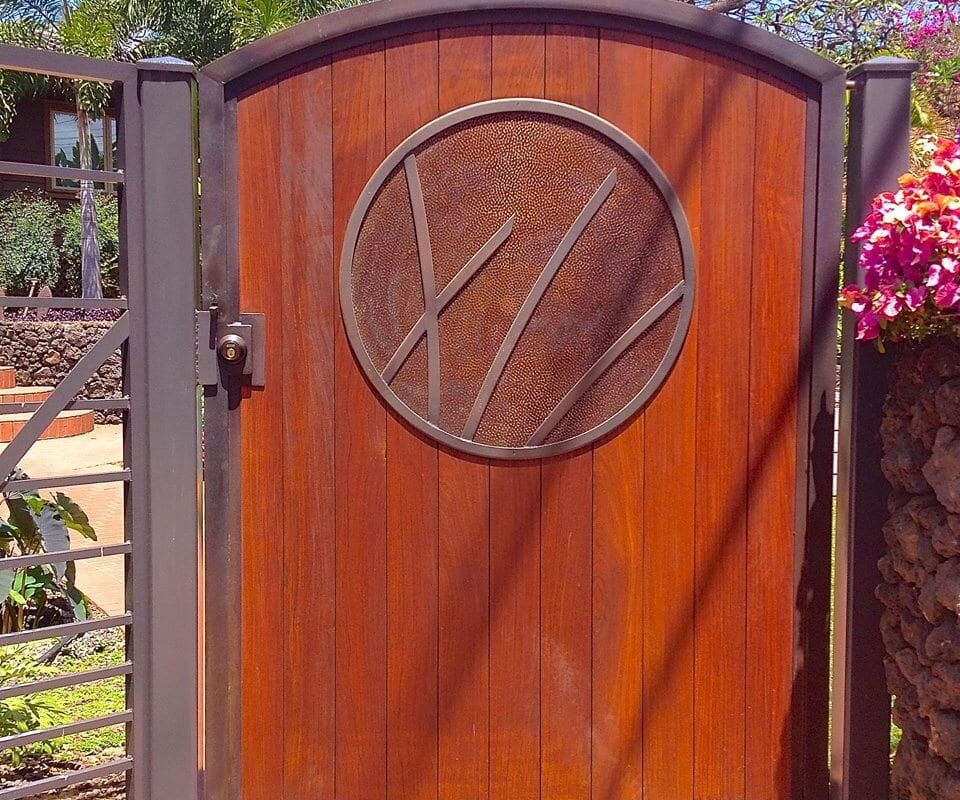 Wooden gate with a circular carved emblem in a garden setting.