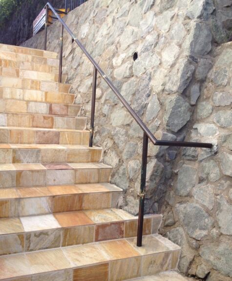 Stone stairs with metal handrail along a textured stone wall.