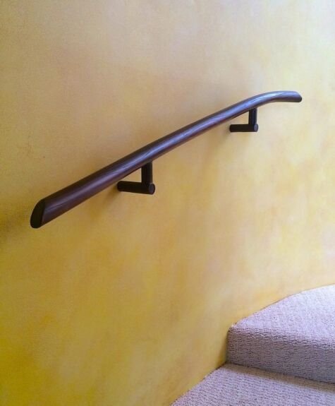 Wooden handrail mounted on a yellow wall beside carpeted stairs.