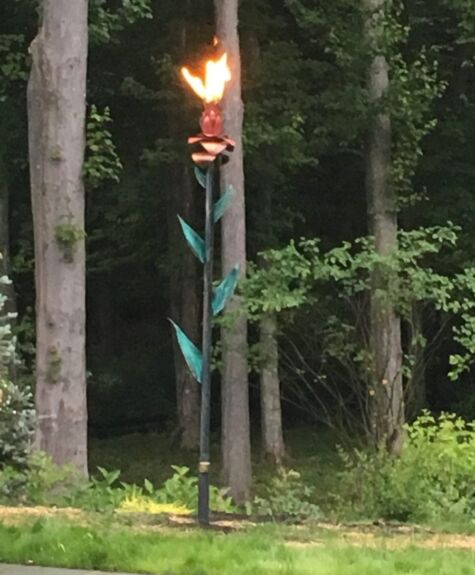 A tall torch with a flame burning at the top in a forest.